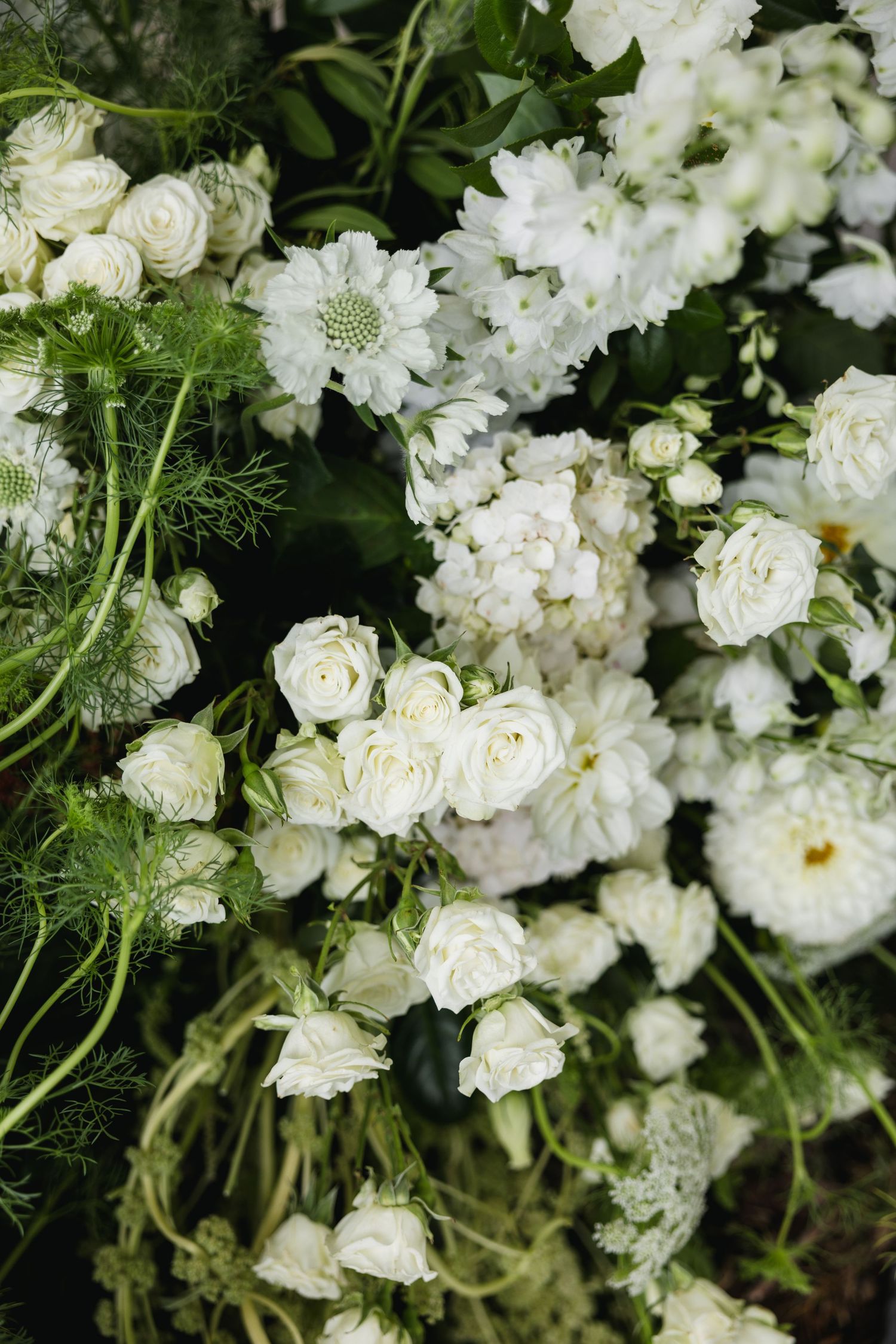 Lush arrangement of white roses and mixed blooms with green foliage for a wedding floral display.