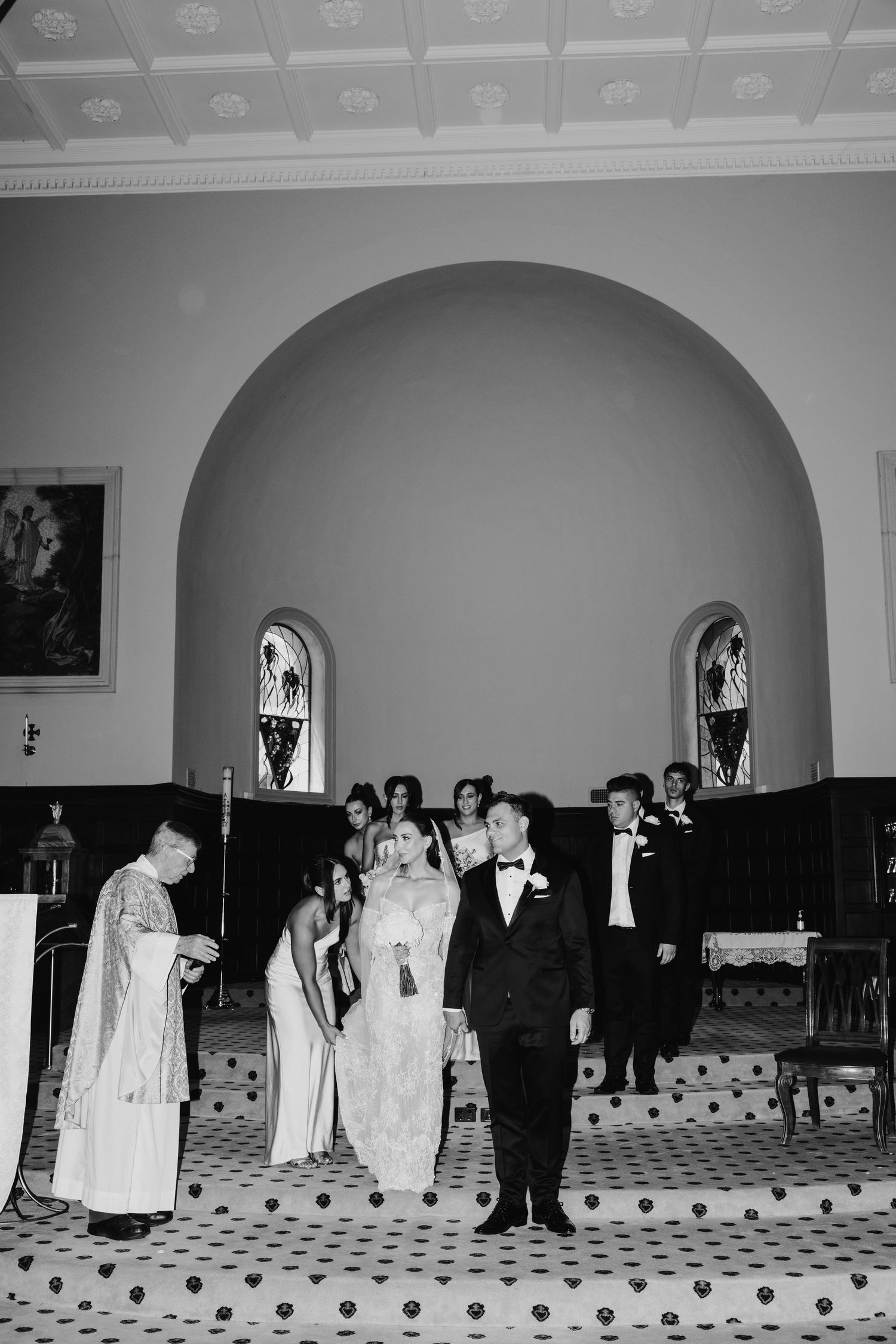 Black and white photo of a wedding ceremony inside a church with bride, groom, and wedding party at the altar.