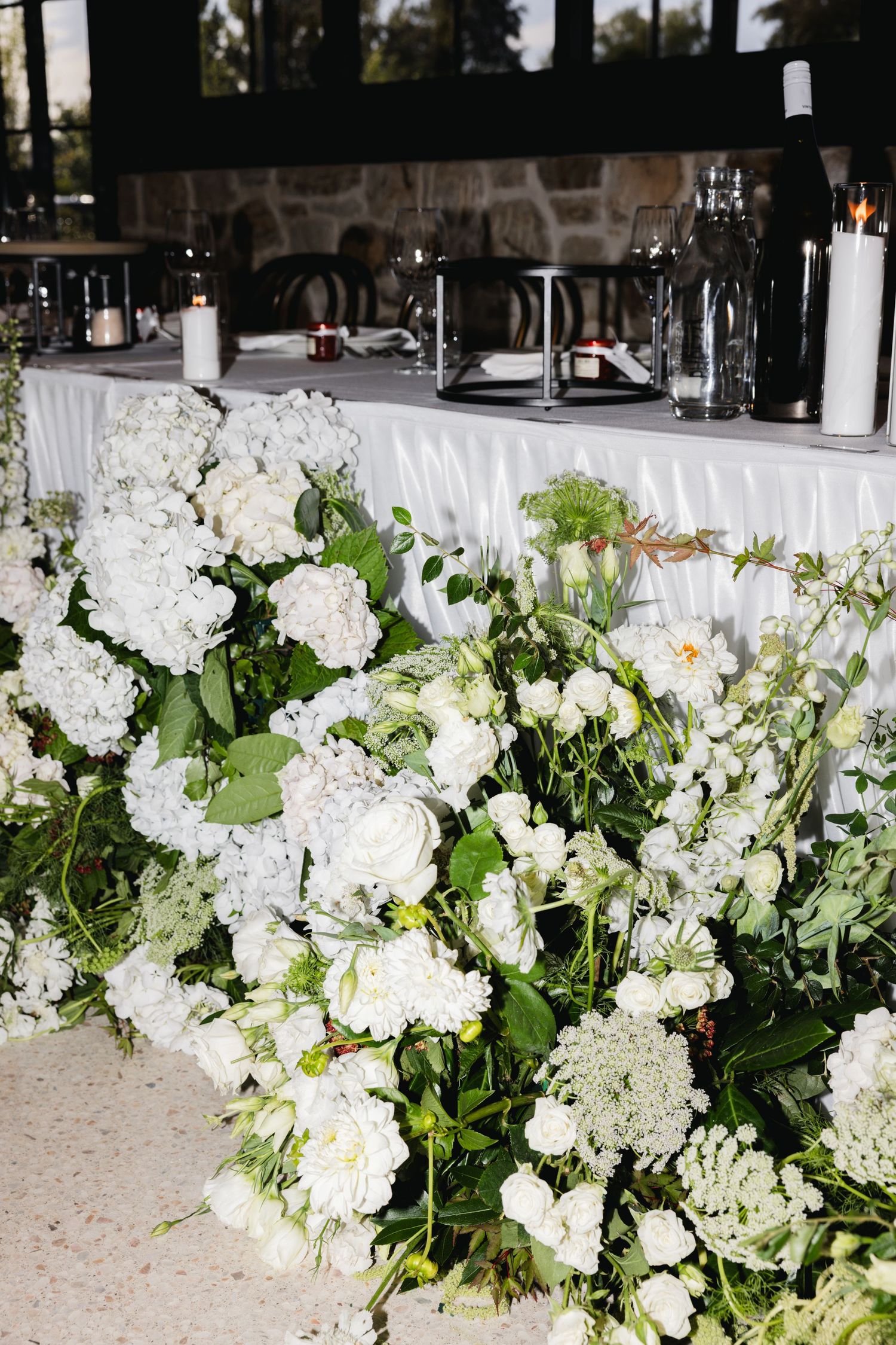 White hydrangea and rose floral arrangements decorating a wedding reception head table with candles.