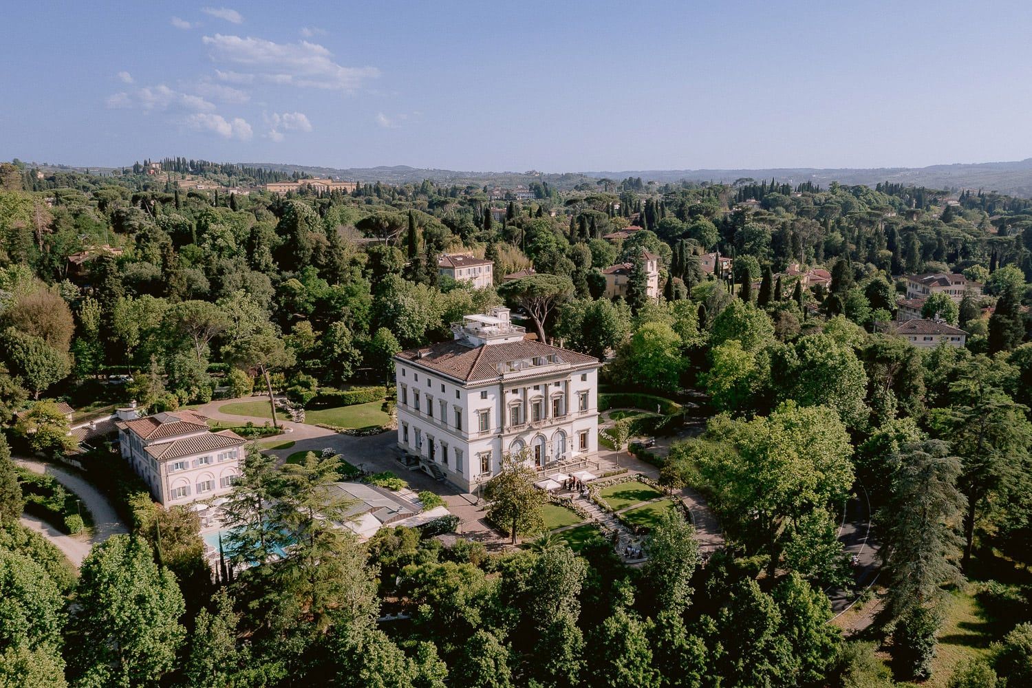 Aerial view of an elegant Italian villa surrounded by manicured gardens and cypress trees.