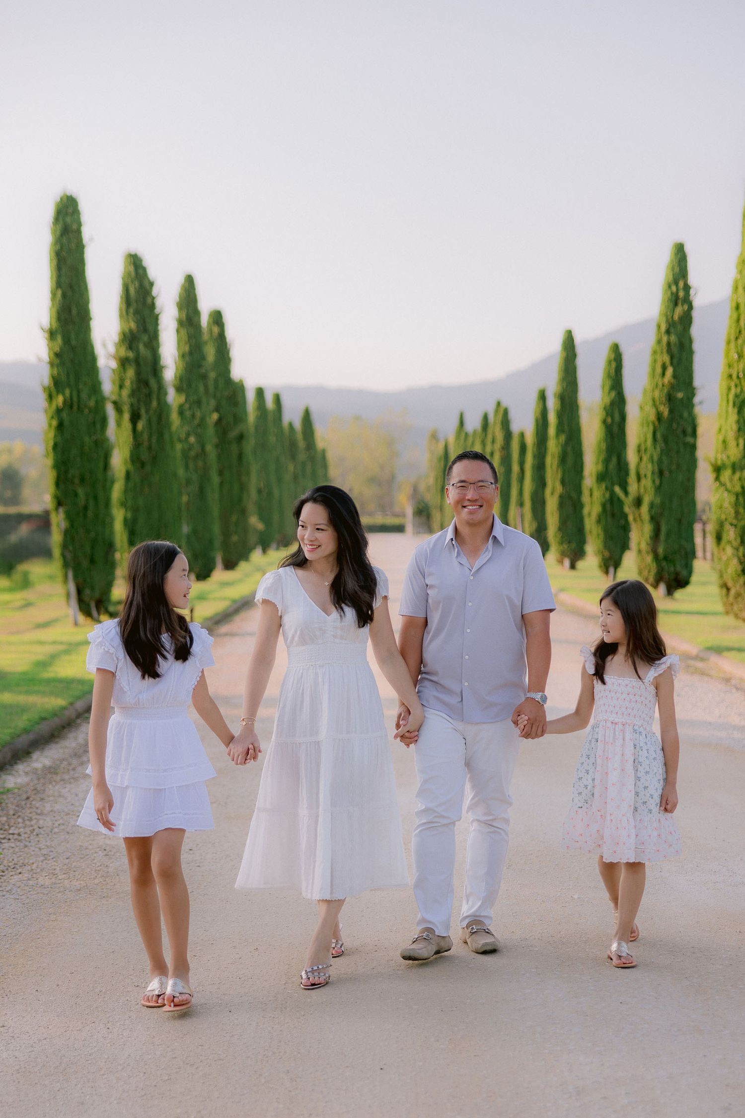 Family group walks along cypress-lined path in coordinated white outfits.