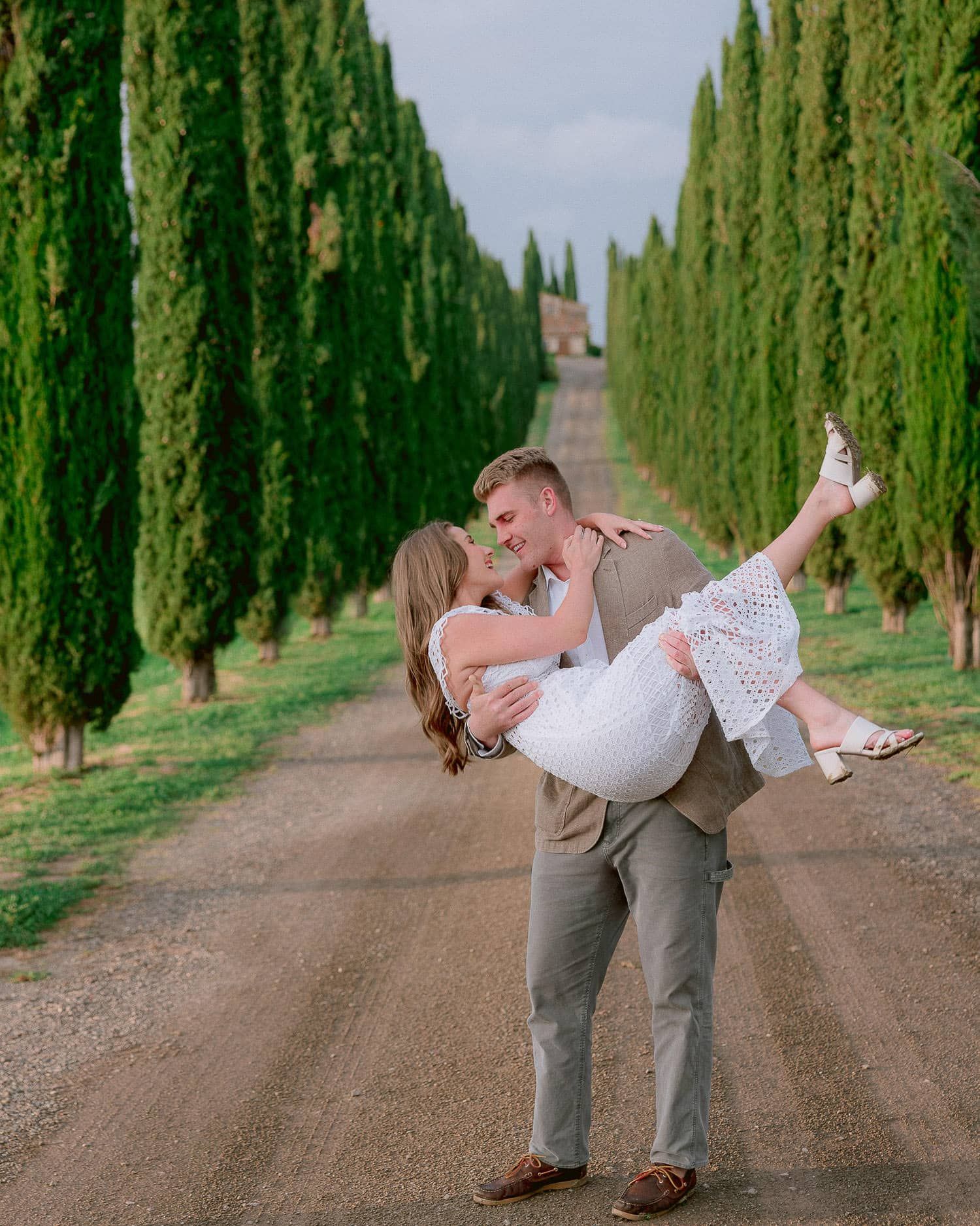 A romantic couple dances playfully along a cypress tree-lined path in Tuscany.