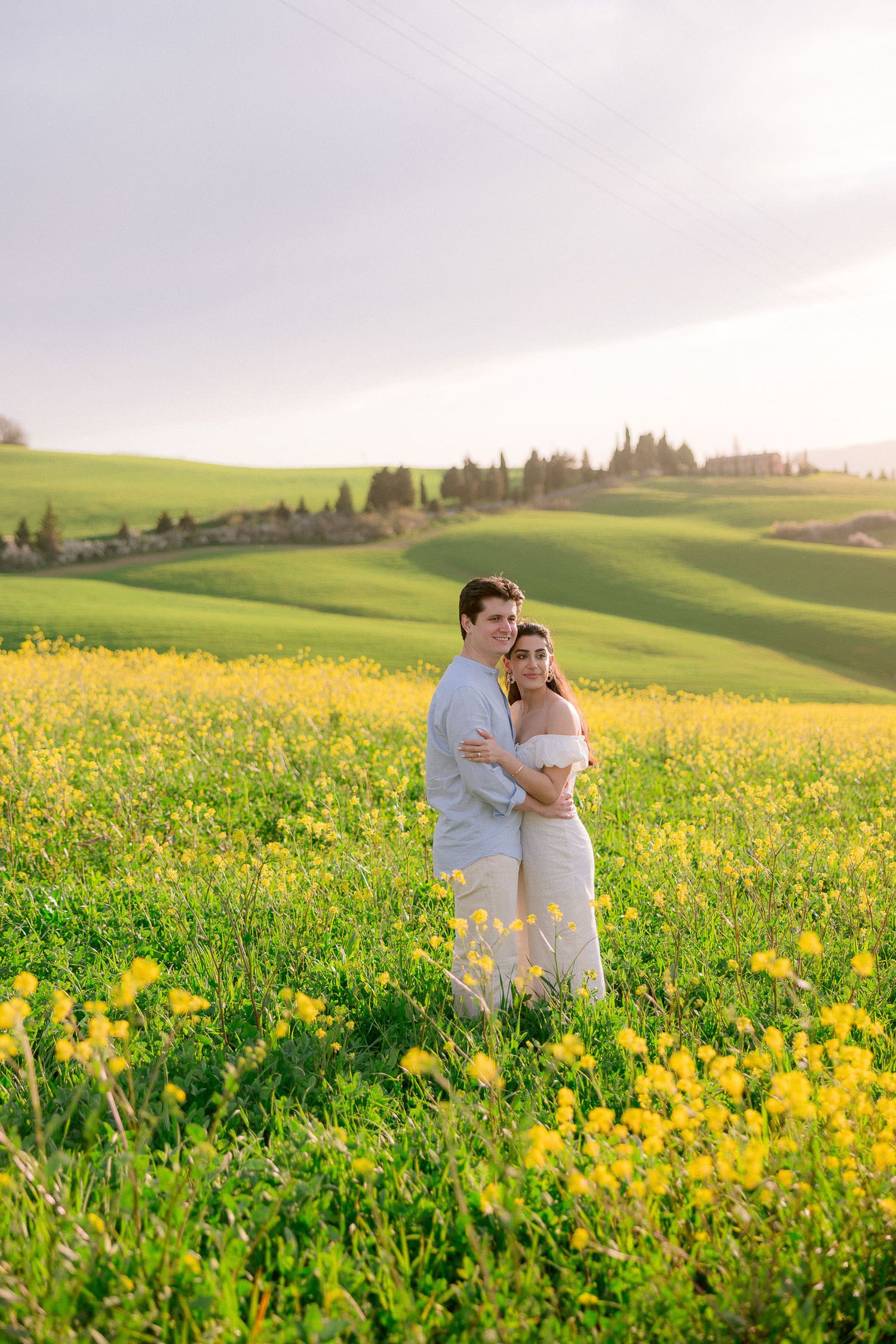 Couple embracing in a field of yellow wildflowers during golden hour in Tuscany.