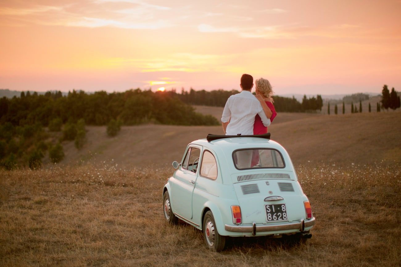 Vintage Fiat 500 parked in Tuscan countryside during golden hour sunset.
