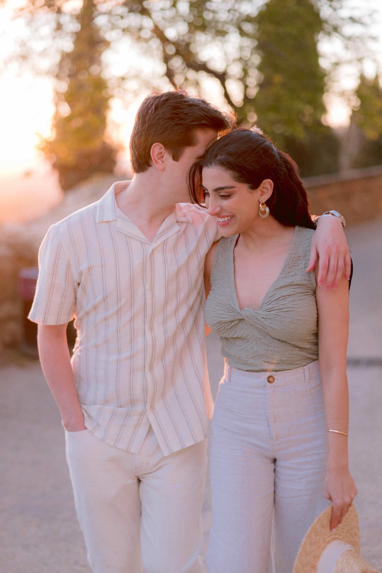 A couple walks together during golden hour wearing light colored casual outfits.