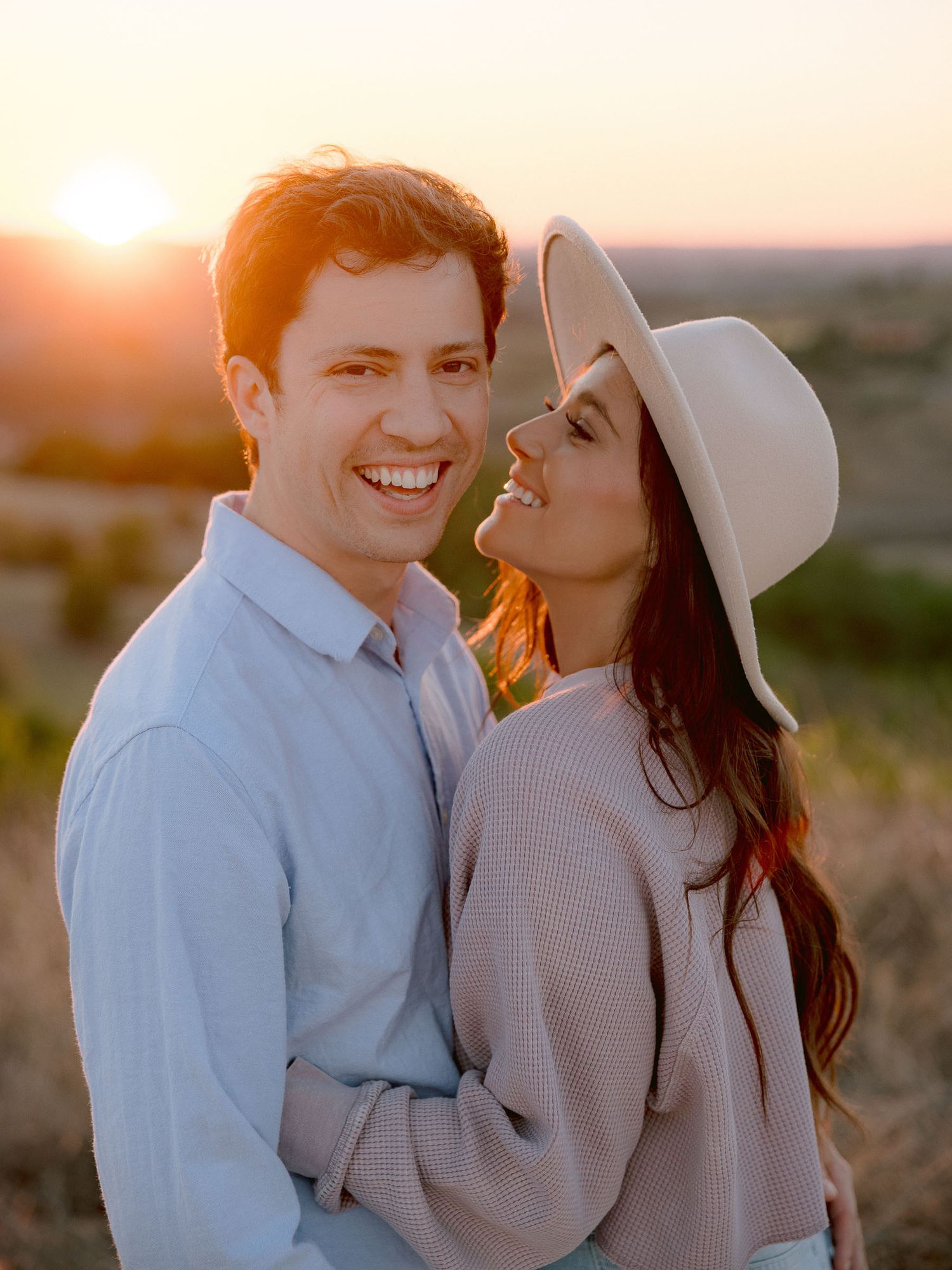 A couple shares a romantic moment at sunset wearing coordinated neutral outfits.