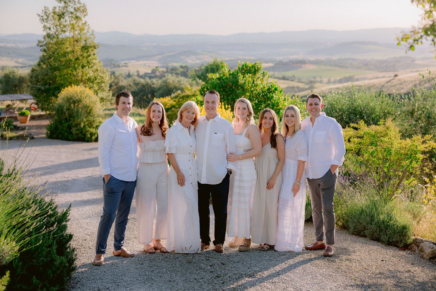 Extended family group photo at sunset in coordinated white and neutral outfits.