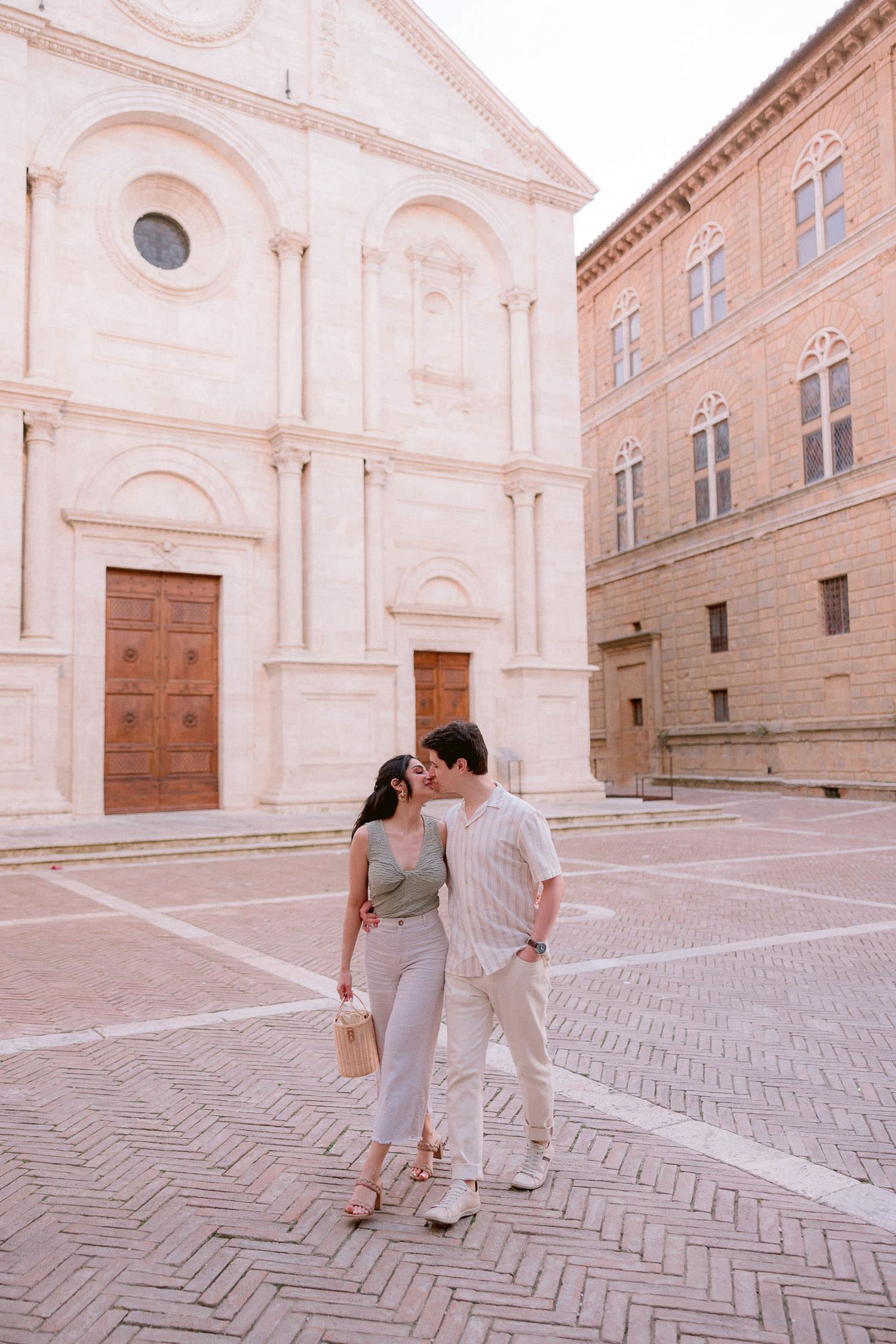 Couple sharing romantic moments in front of an ornate Italian church with herringbone brick pavement.