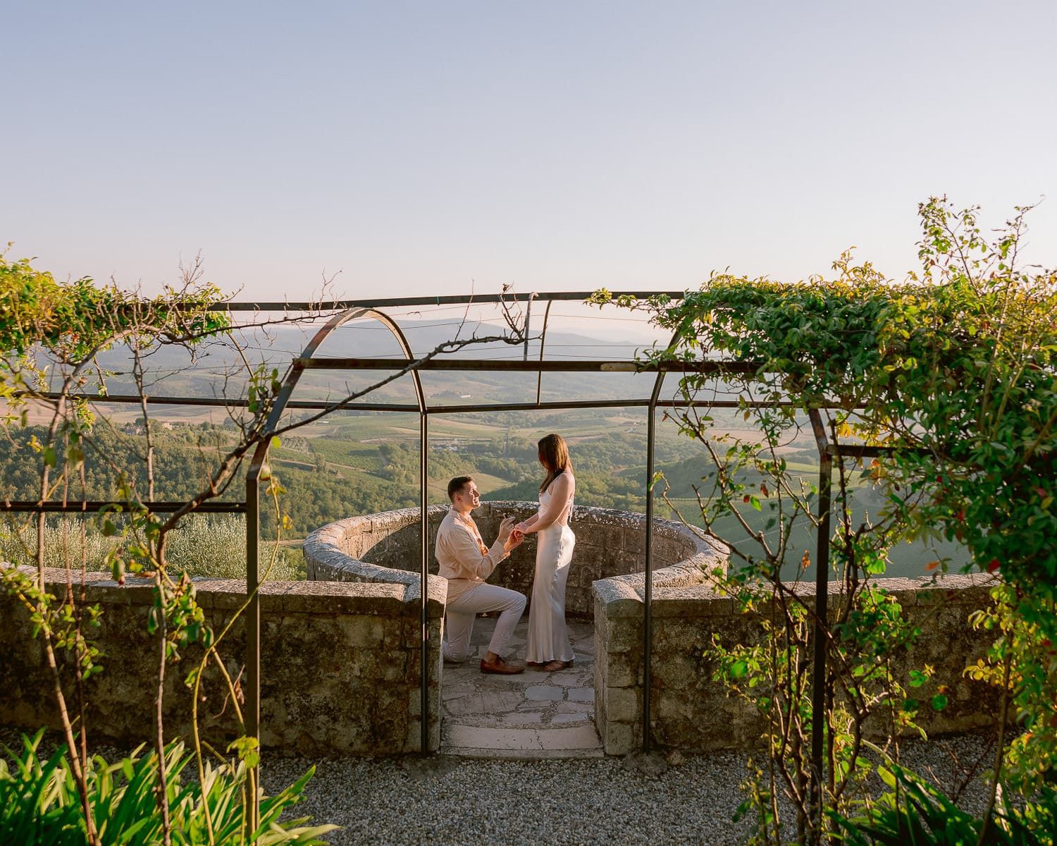 Stone terrace with wrought iron details overlooking the scenic Tuscan countryside at sunset.