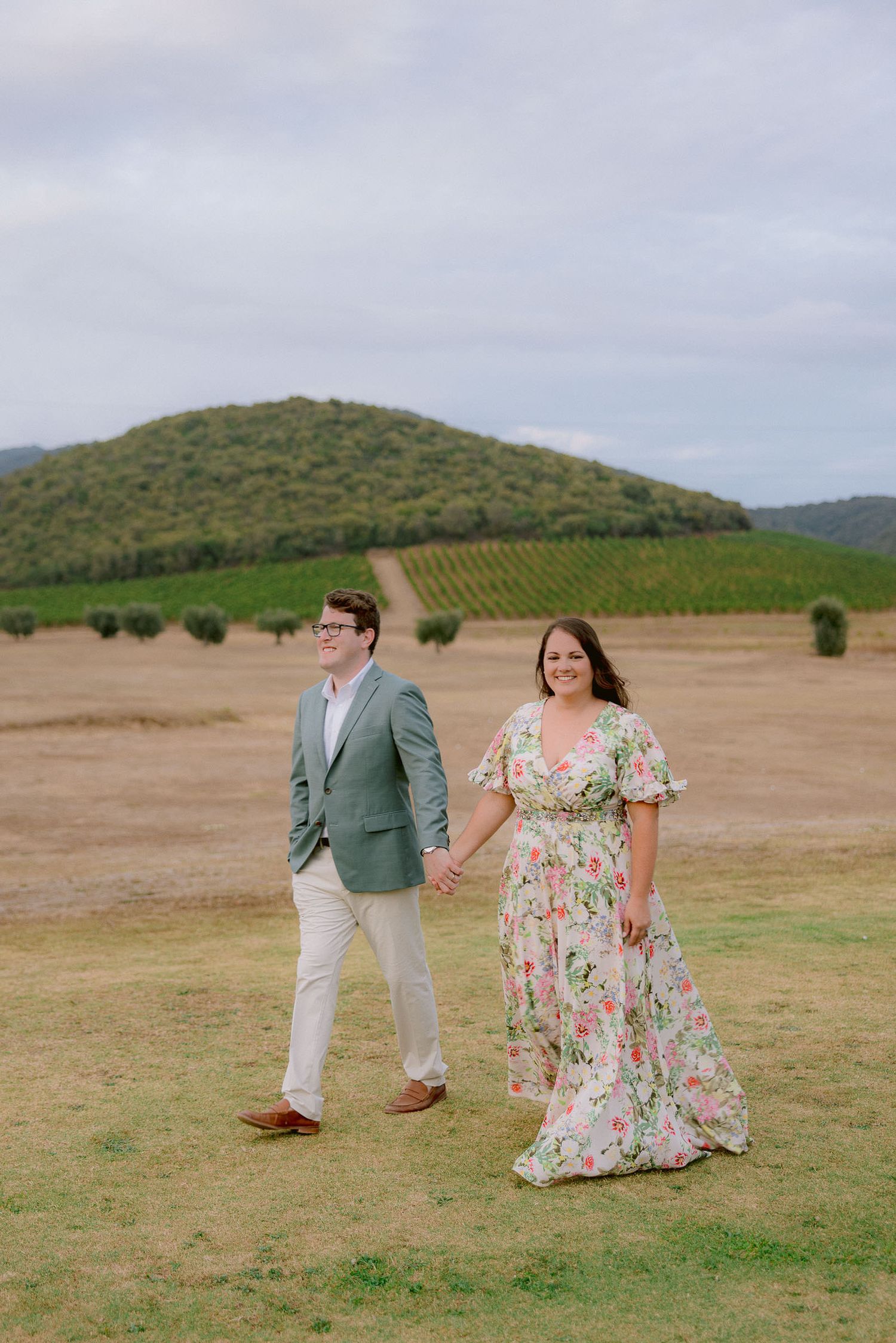 Couple in spring attire walking through a scenic hillside landscape.