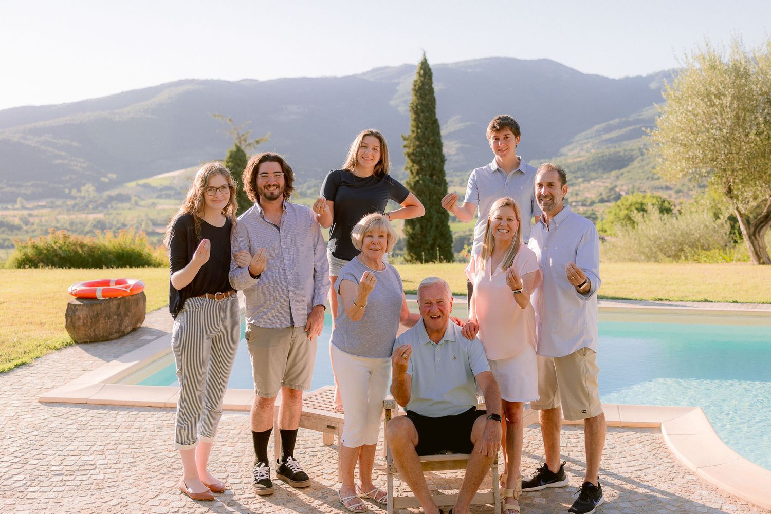 Extended family portrait by pool with mountains and cypress trees in background.