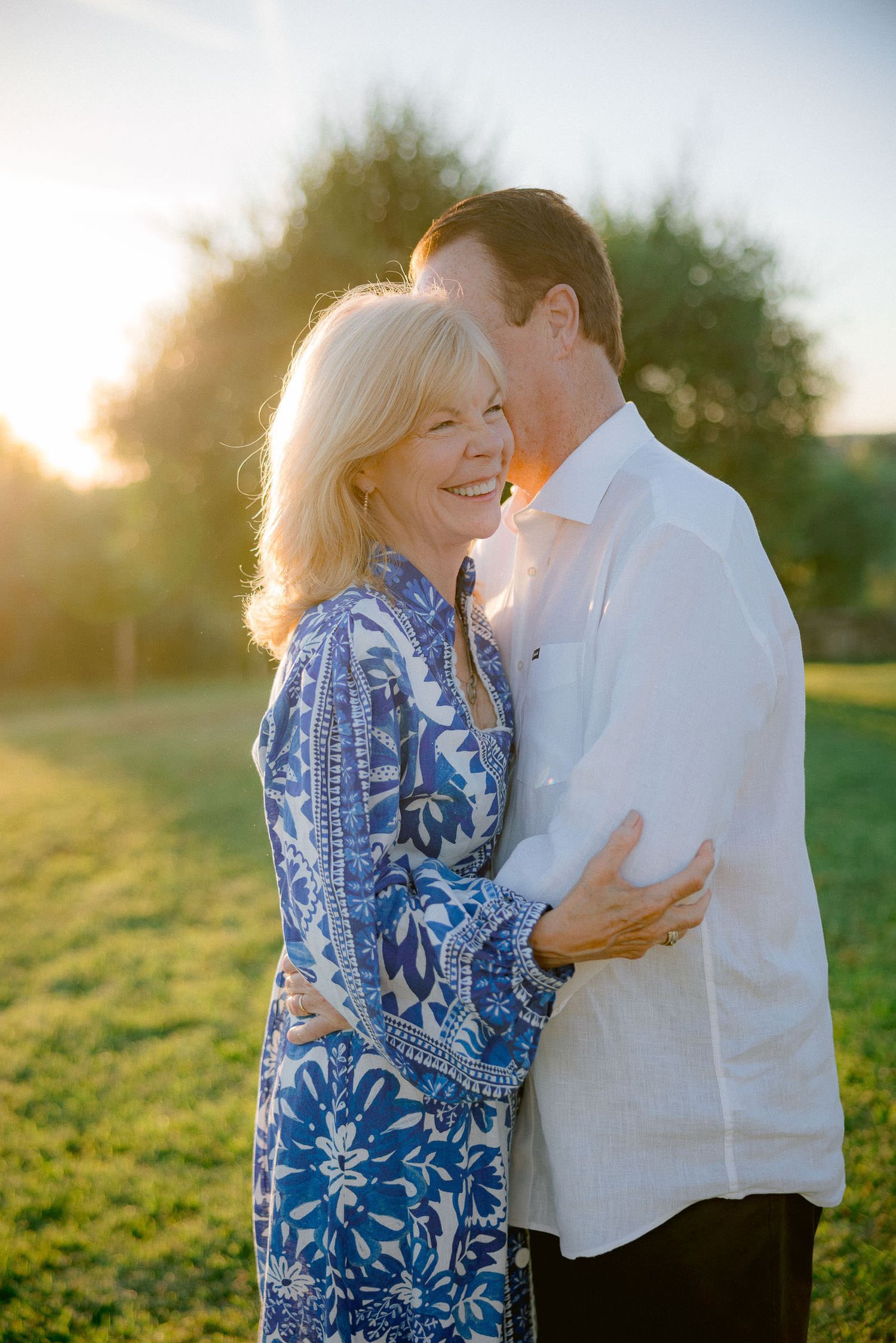 Couple shares intimate moments while laughing together in a sunlit field.