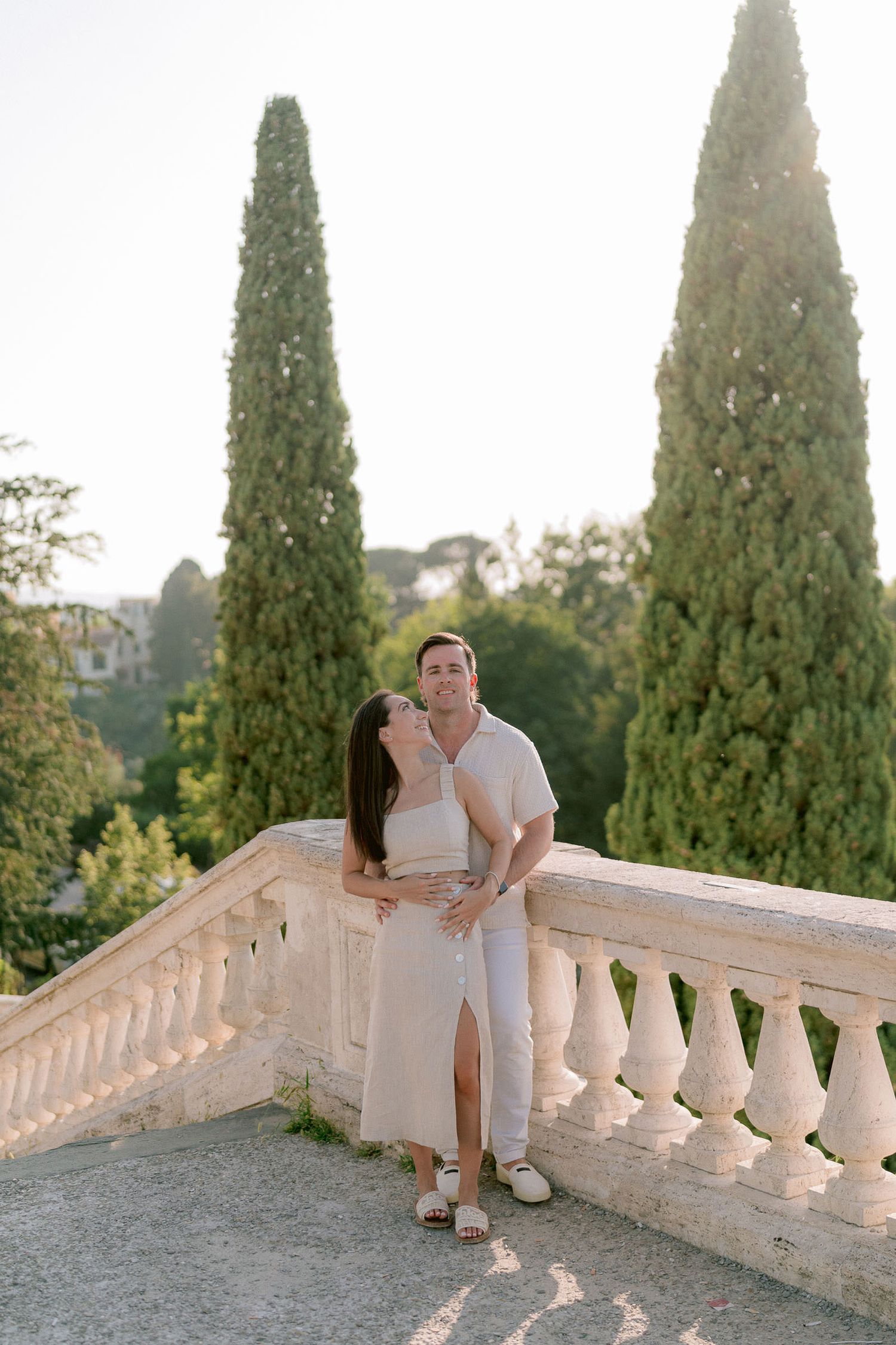 A couple shares an intimate moment on a classic stone balustrade in a Mediterranean setting.