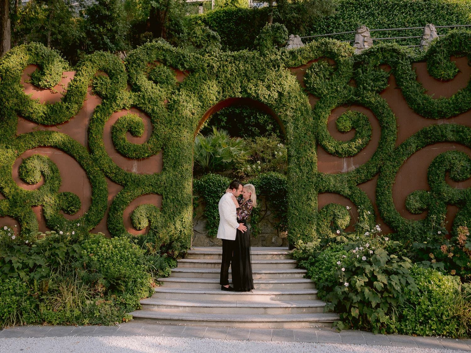 Garden pathway with ornate hedge designs and flowering plants creates a romantic setting.