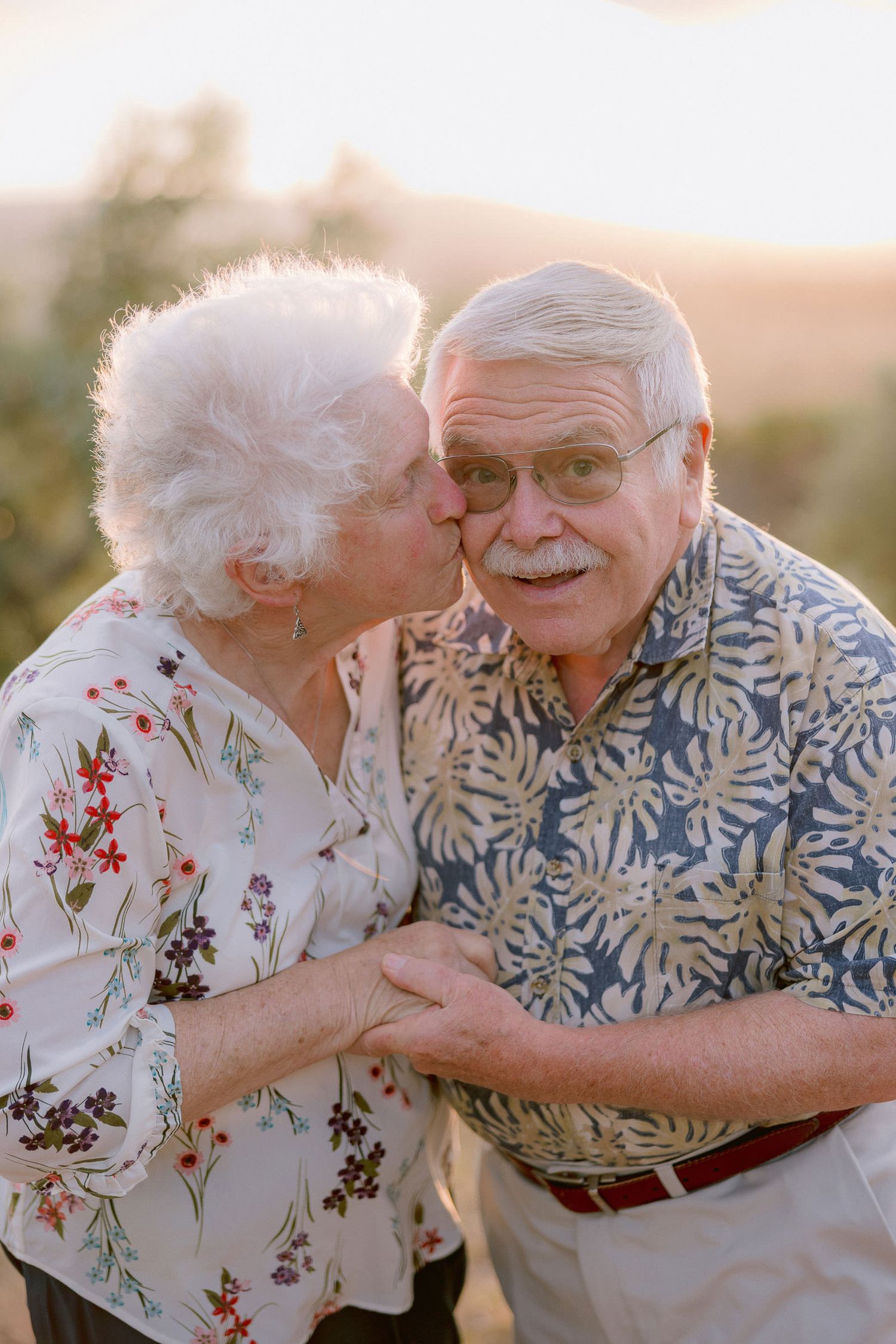 Tender moment between a couple in floral and tropical print shirts during sunset.