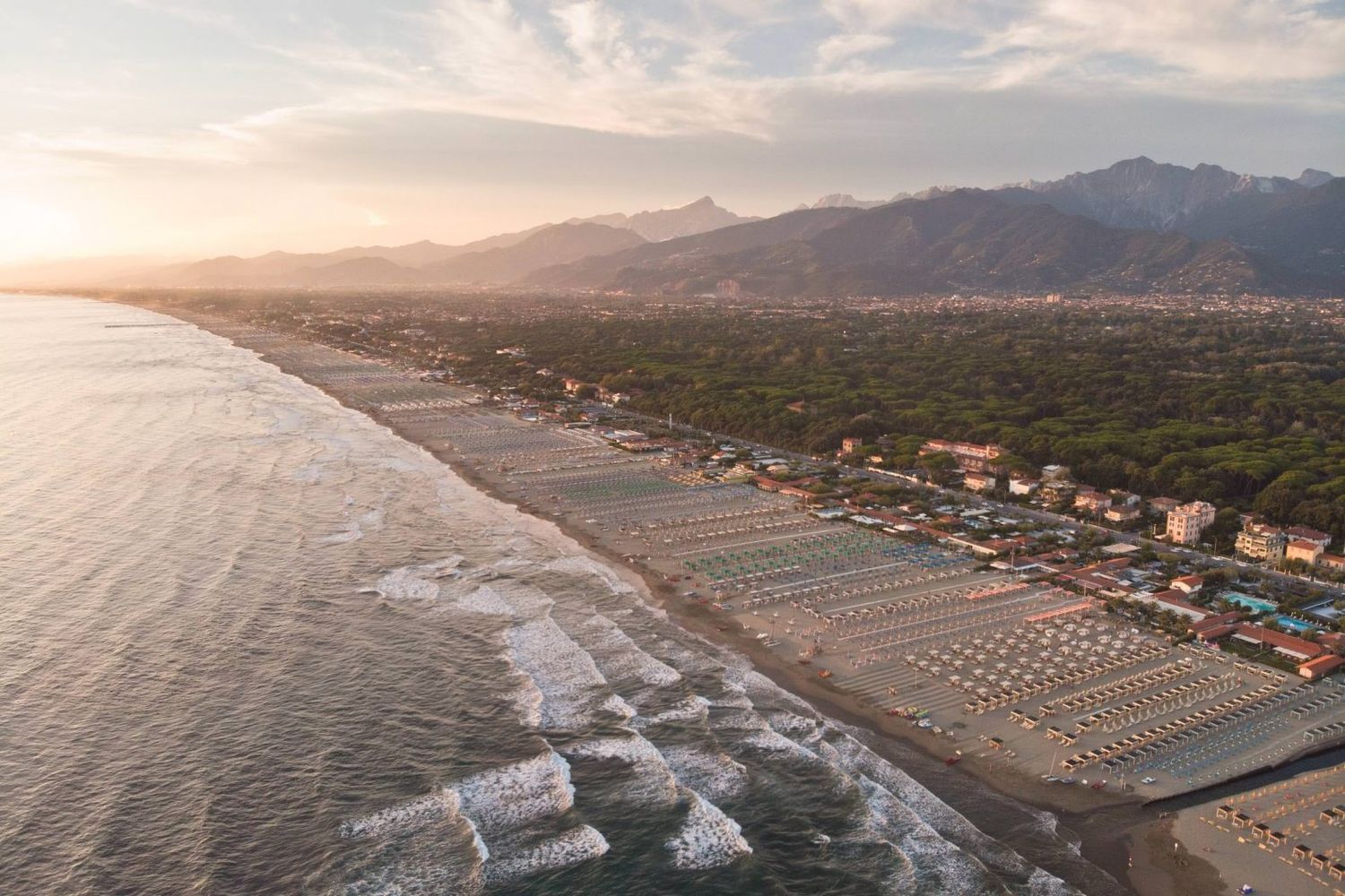 Aerial view of a Mediterranean beach resort with umbrellas and buildings along the coastline.