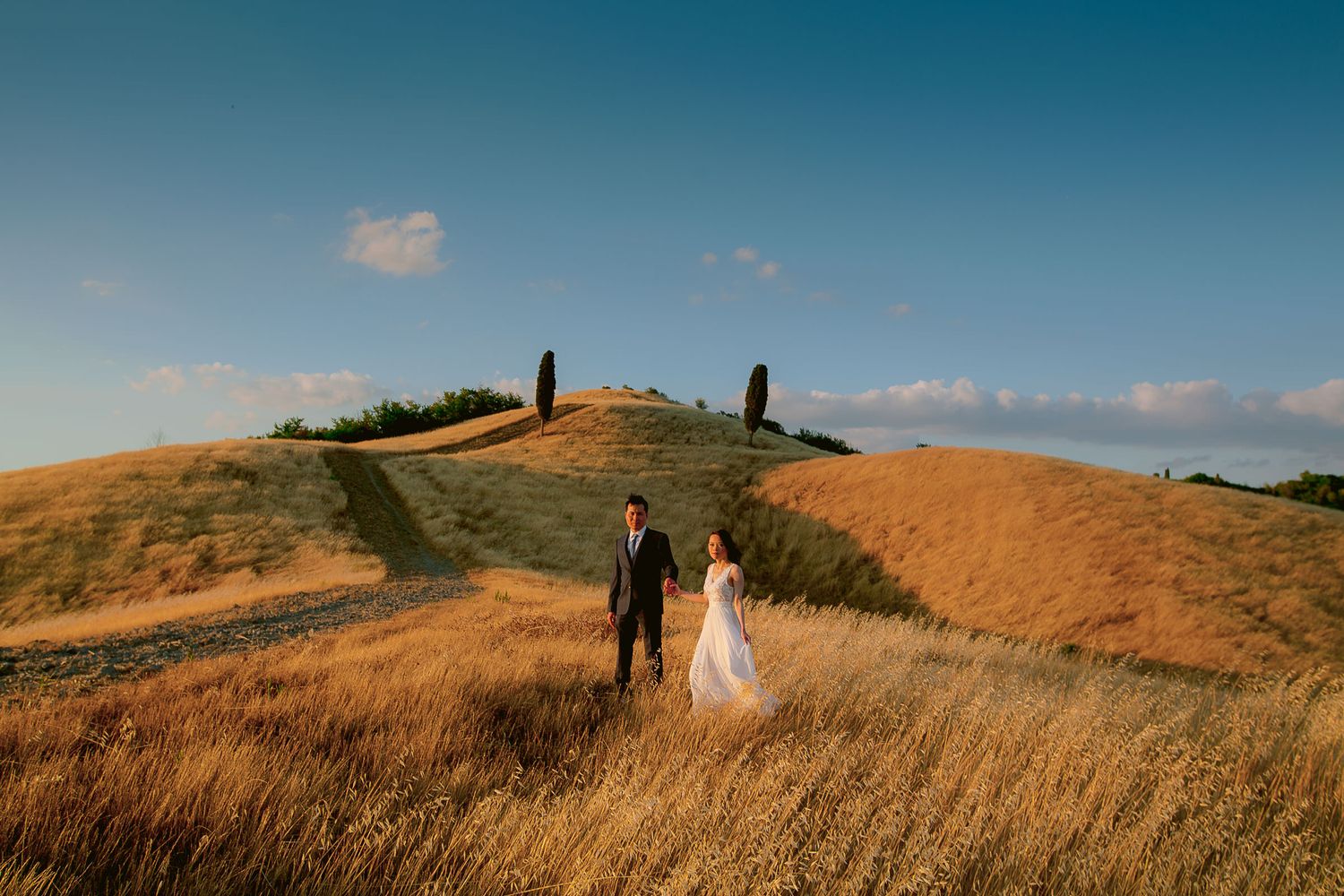 Silhouettes walking through golden wheat fields at sunset with mountains in background.