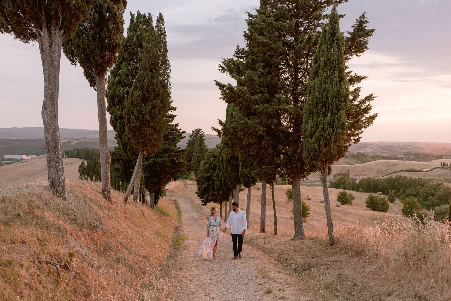 A scenic pathway lined with tall cypress trees at sunset in Tuscany.