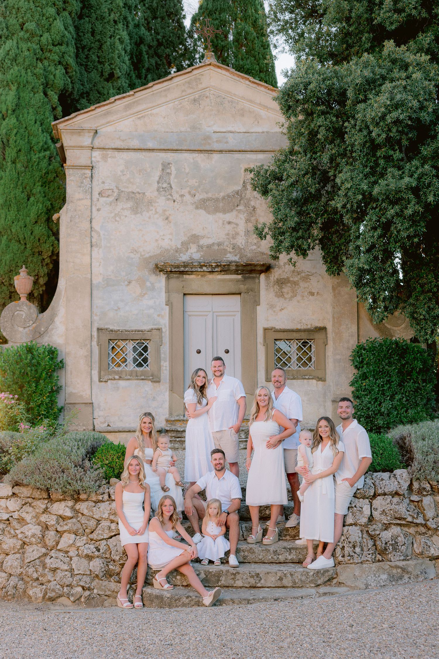 A group poses on stone steps in front of a historic Italian villa surrounded by cypress trees.