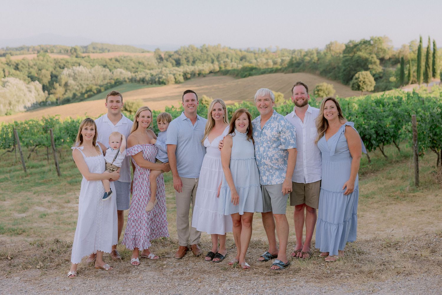 Extended family portrait in pastel outfits against vineyard landscape.