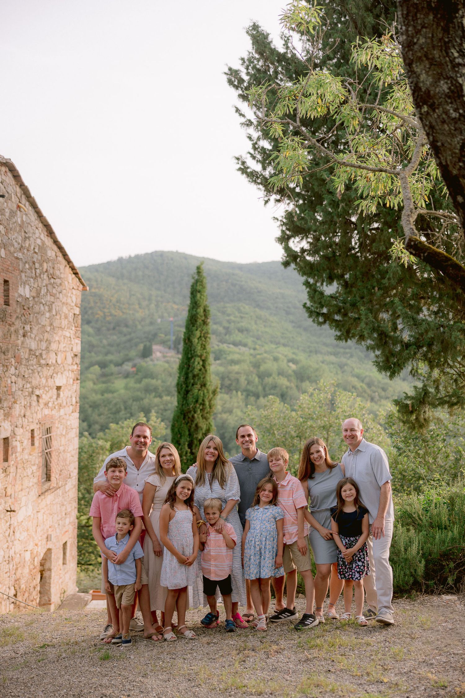 Extended family poses together outside a rustic stone villa in the Tuscan countryside.