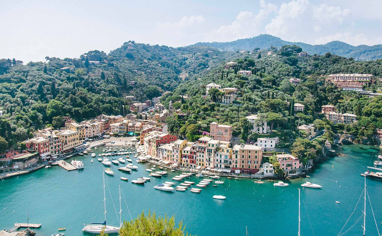 Panoramic view of a Mediterranean harbor with colorful buildings and boats along the coastline.