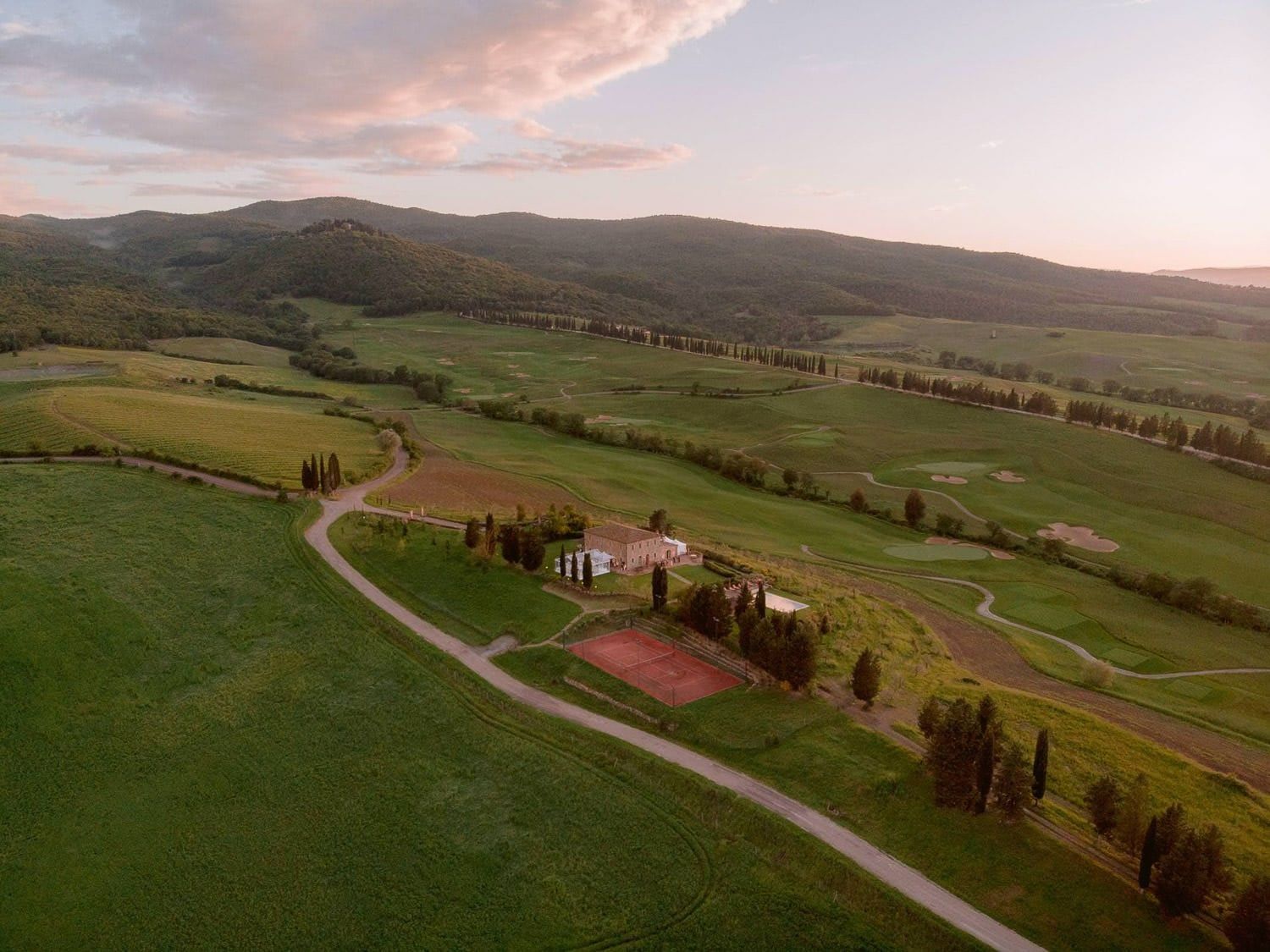Rolling hills of Tuscany stretch into the distance with a villa and cypress trees dotting the landscape.