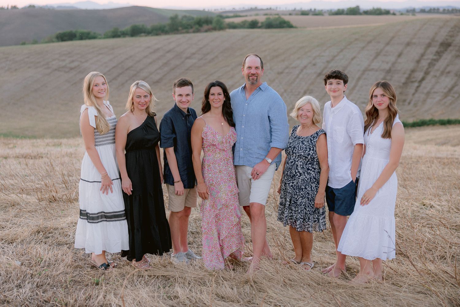 Family group photo in coordinated outfits against rolling Tuscan hillside.