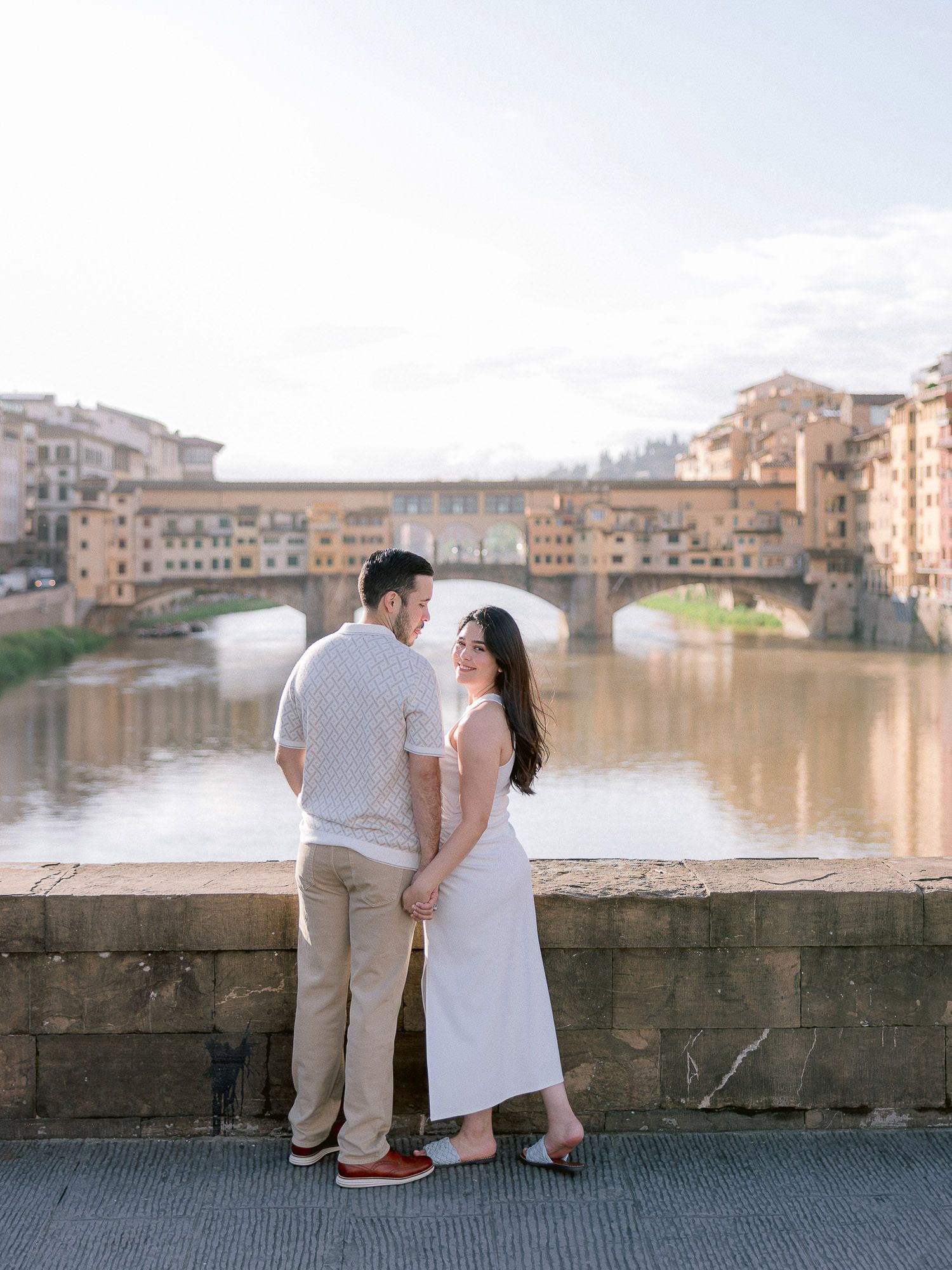 Romantic couple enjoys sunset views along the historic Ponte Vecchio bridge in Florence, Italy.