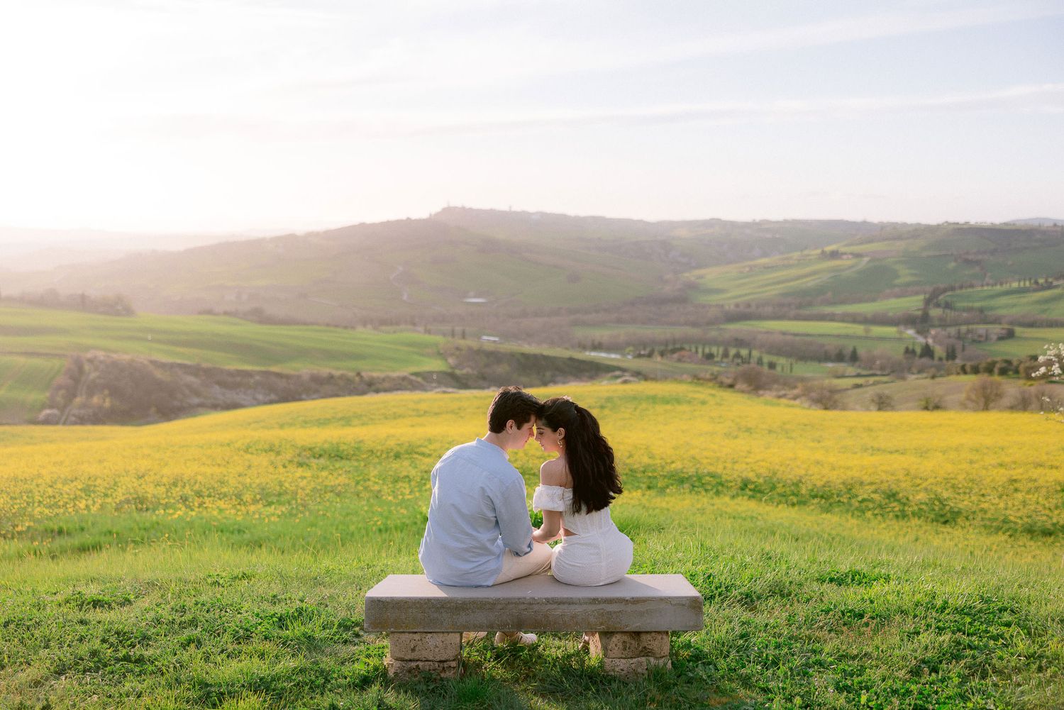 A couple enjoys a tender moment in a flowering meadow with rolling hills in the background.
