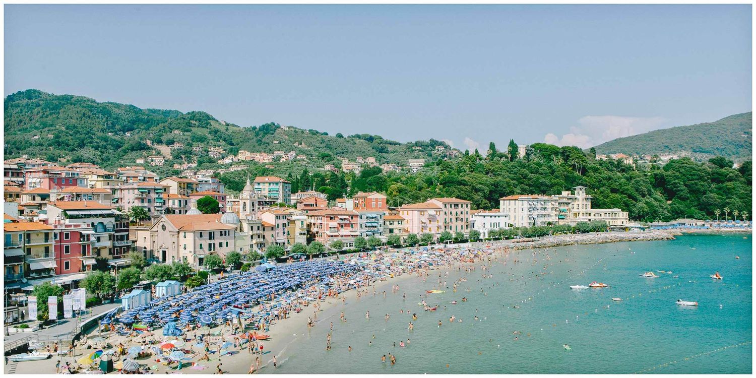 Coastal panorama of an Italian Riviera town with boats dotting the blue Mediterranean waters.
