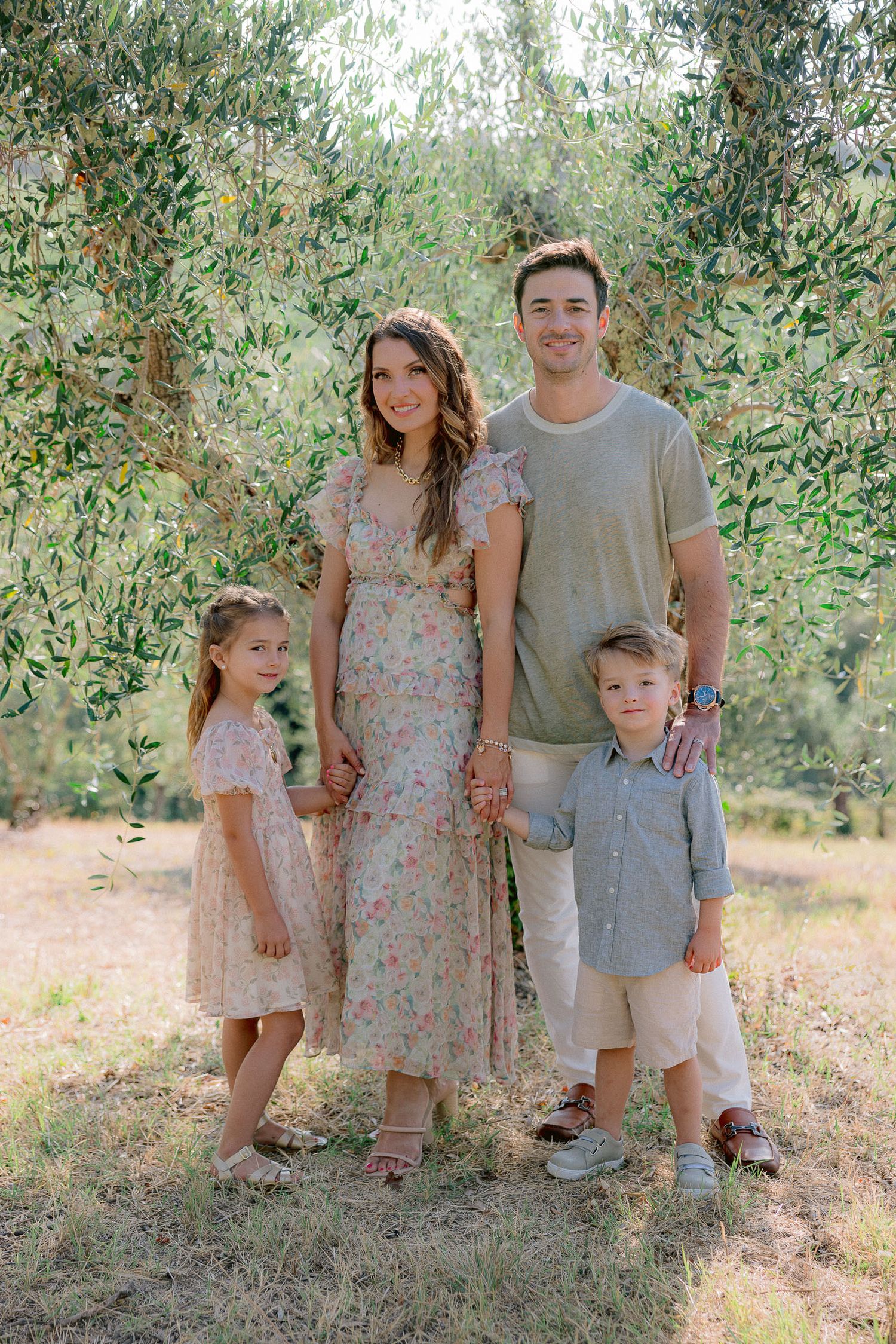 Family portrait session in an olive grove wearing coordinated floral and neutral outfits.