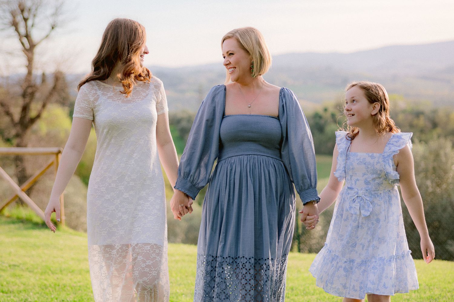 Three people in blue and white dresses walk together in a sunny outdoor setting.