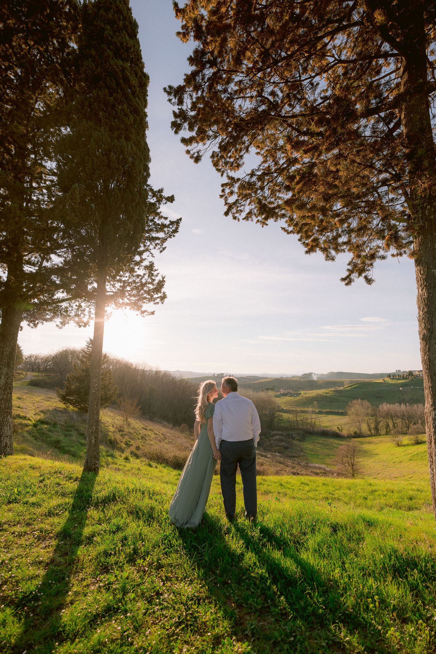 Romantic sunset moment among cypress trees on rolling green Tuscan hillside.