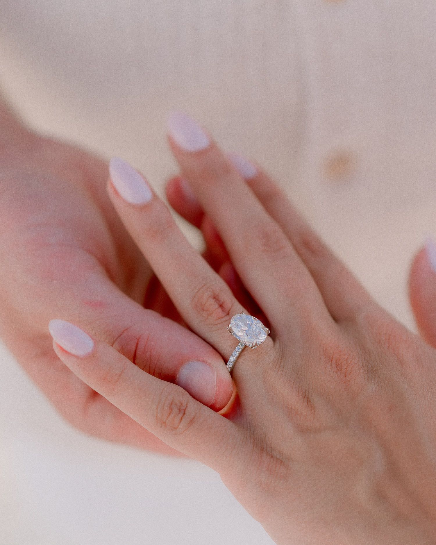 Close-up of a sparkling diamond engagement ring on a delicate hand with pink manicure.