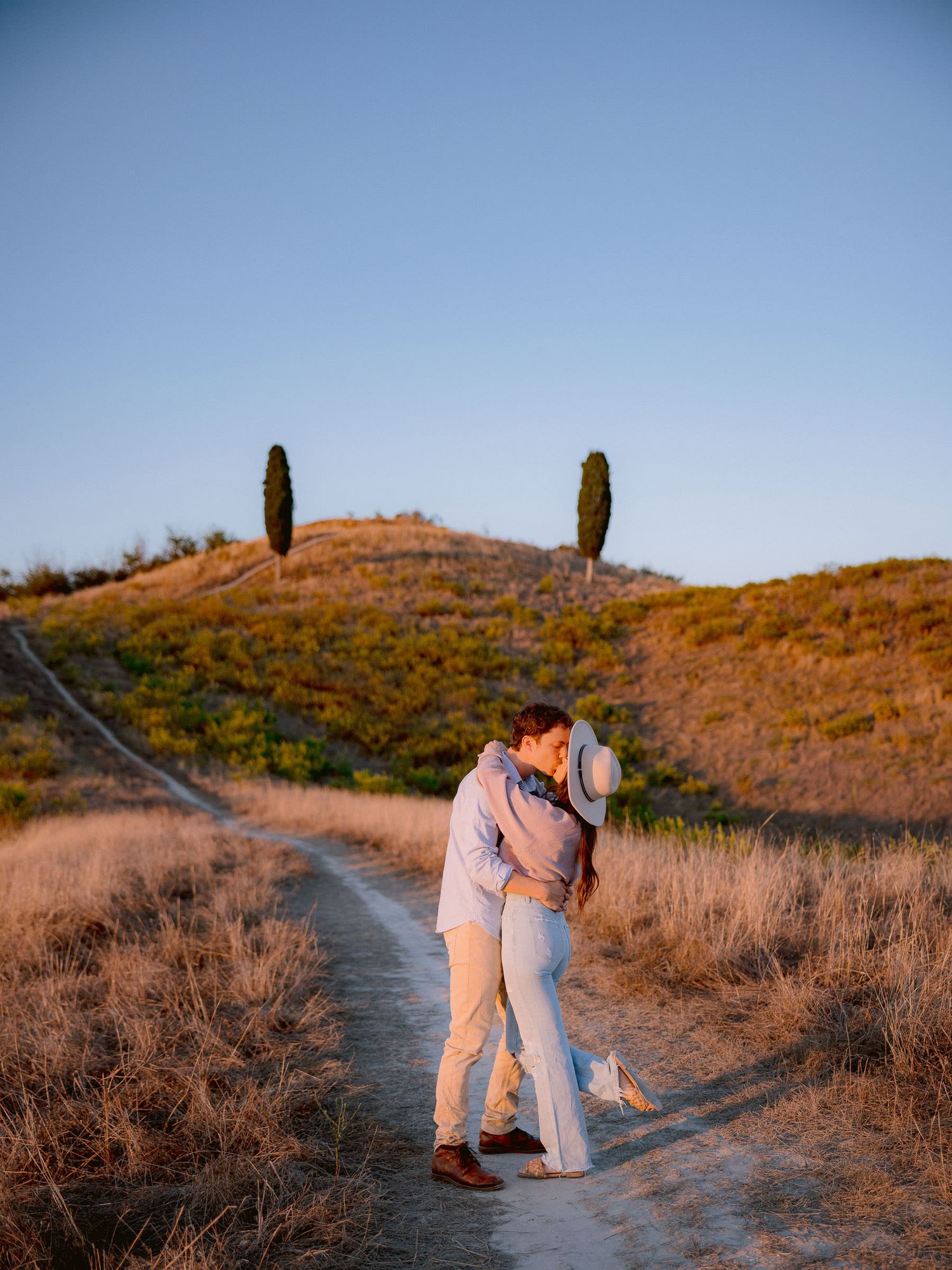 A couple shares a romantic moment on a hilltop trail during golden hour.