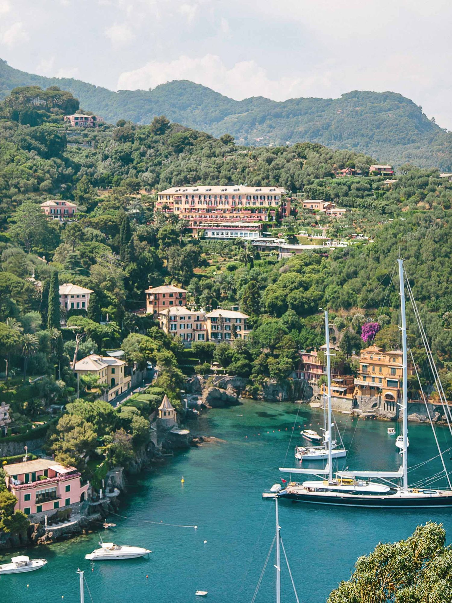 Luxury yachts and sailboats moored in a picturesque Italian harbor surrounded by hills.