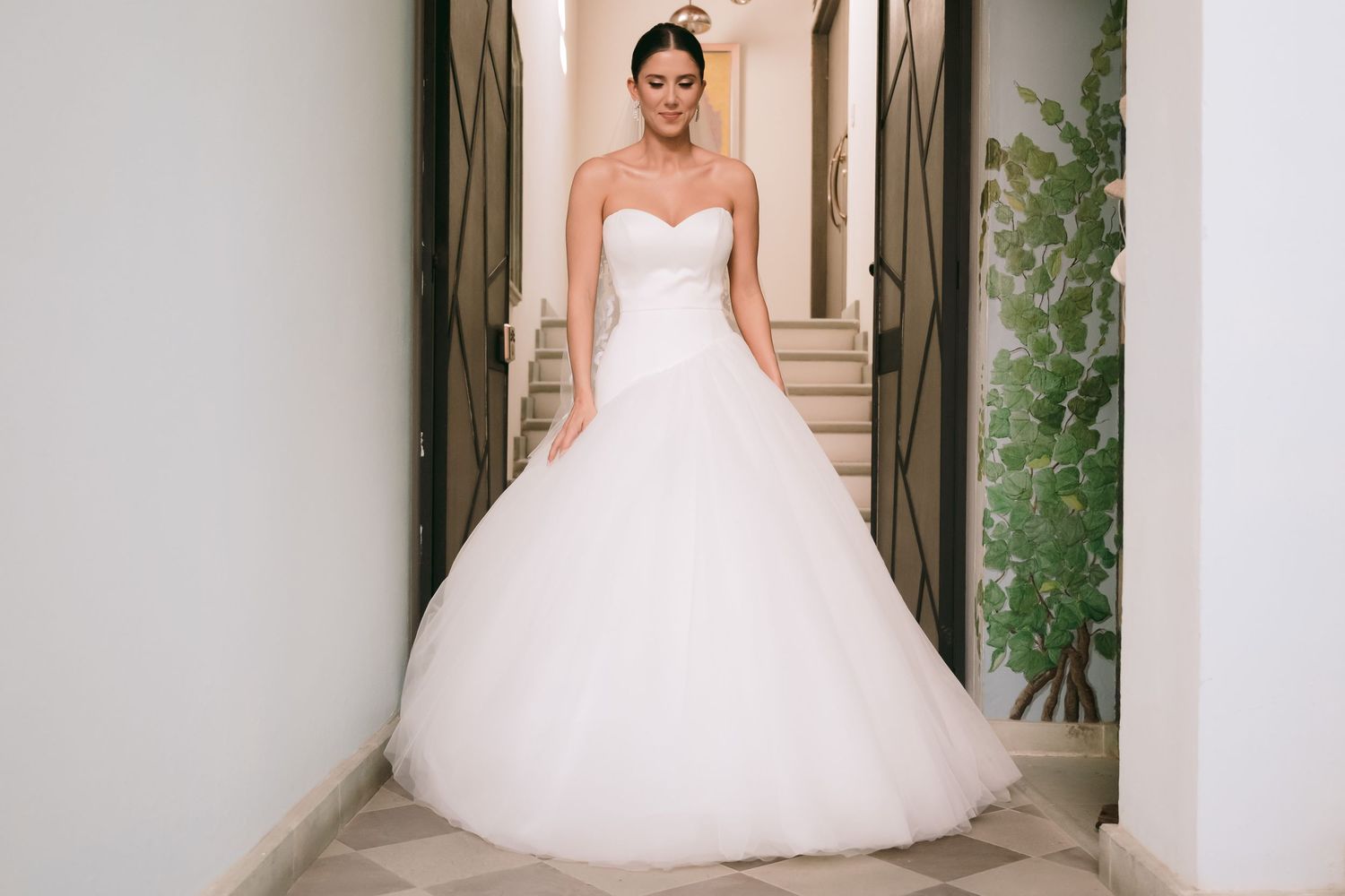 Bride wearing a strapless sweetheart ballgown wedding dress with a full tulle skirt, standing in an elegant hallway.