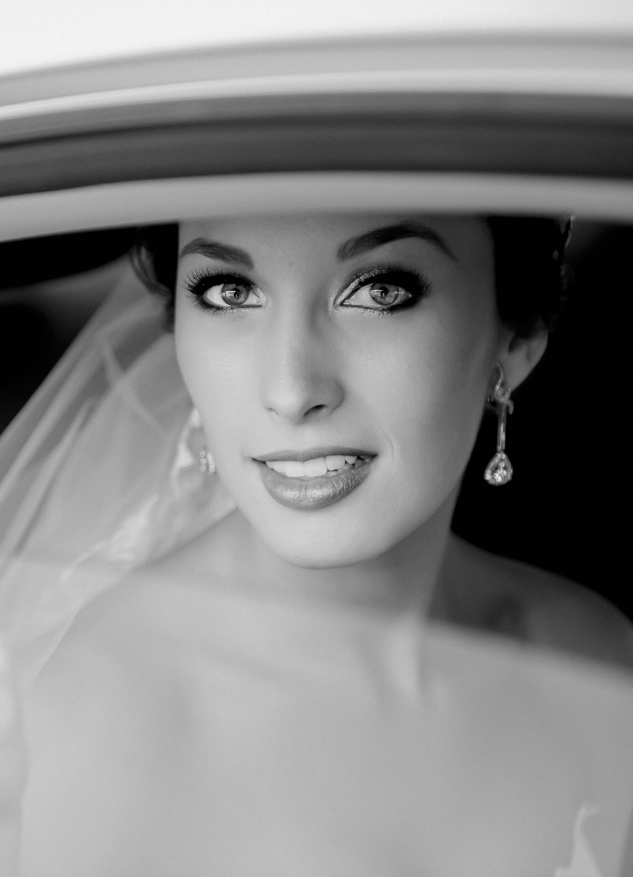 Artistic black and white bridal portrait captured through the frame of a car window.
