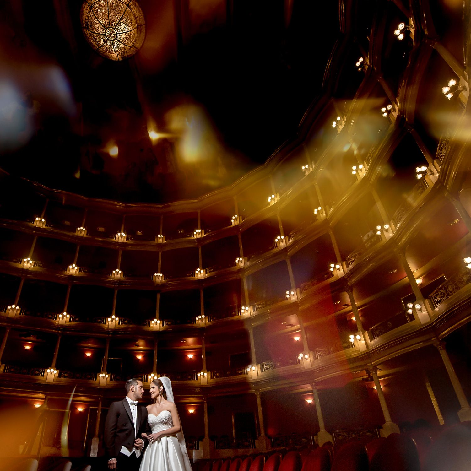 Wedding couple standing beneath ornate theater balconies with warm glowing lights.