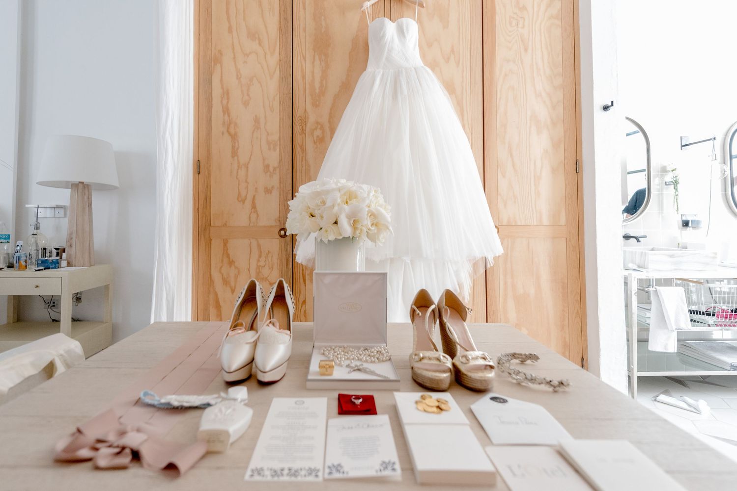 Wedding accessories including shoes and dress laid out on light wooden flooring.