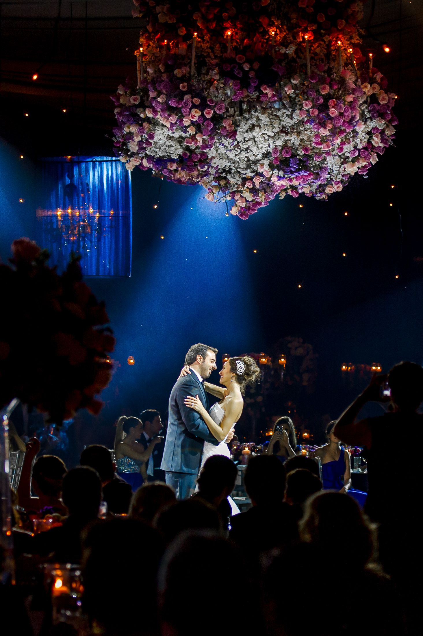 First dance under hanging floral installation with dramatic blue lighting.