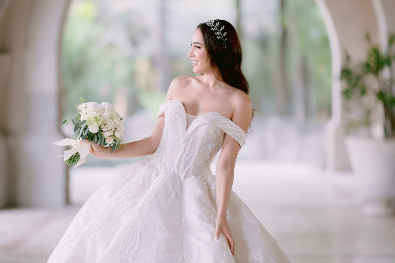Side profile of bride in luxurious ball gown against ethereal outdoor backdrop.