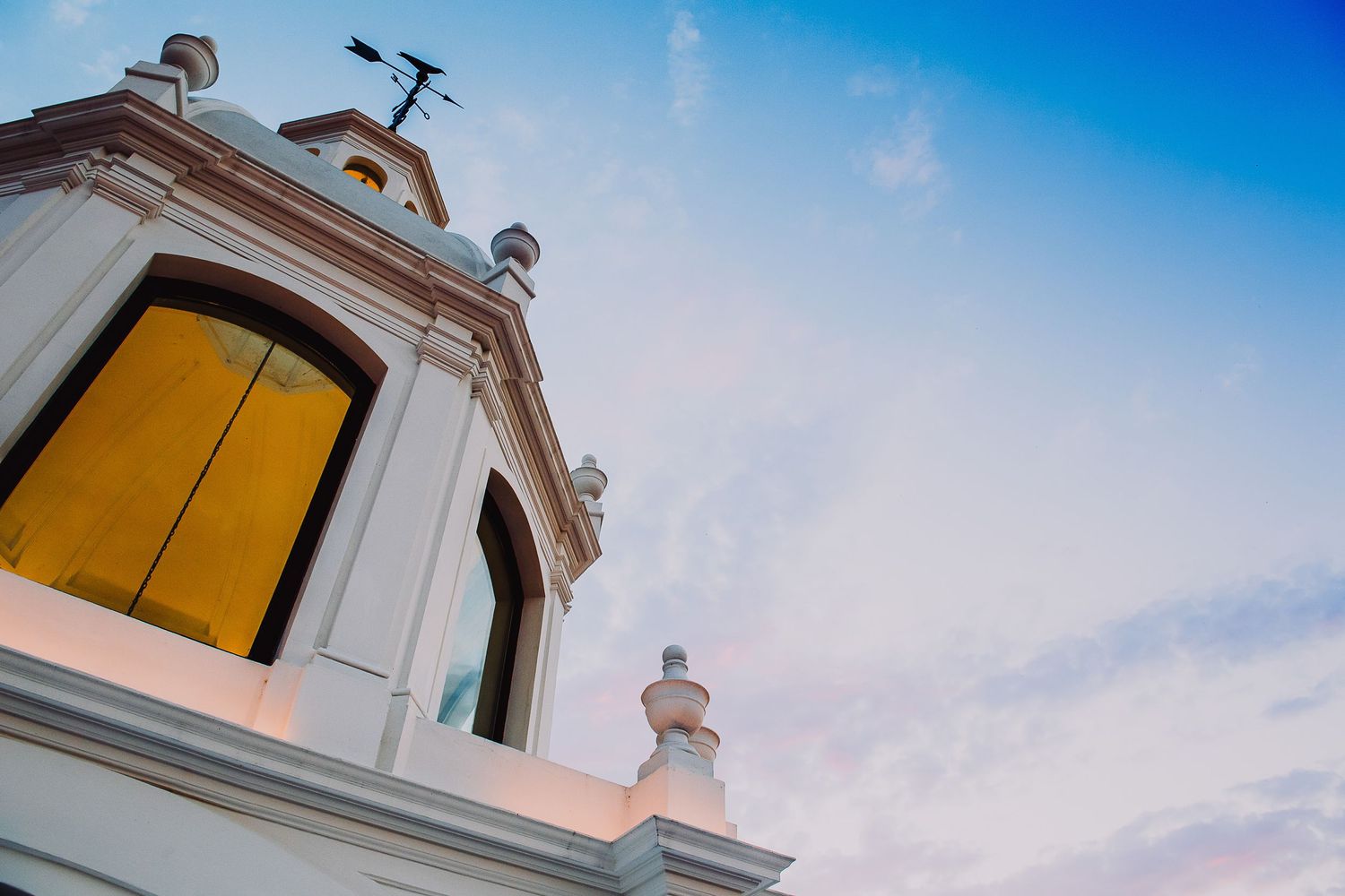 White colonial church bell tower with golden doors against a blue sky at dusk.