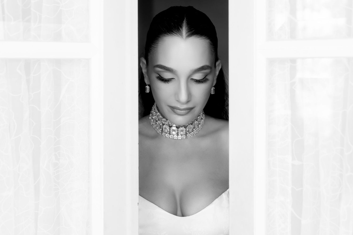 Black and white portrait of a person wearing an ornate choker necklace and white top with eyes closed.