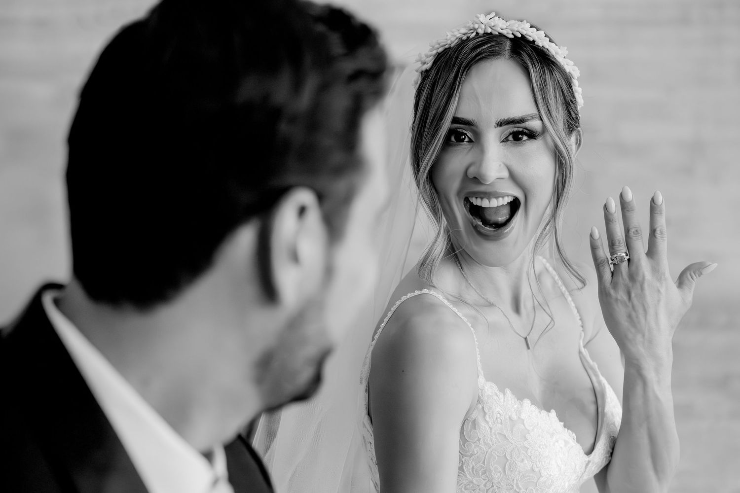 Black and white photo of a joyful bride showing her ring to the groom on their wedding day.