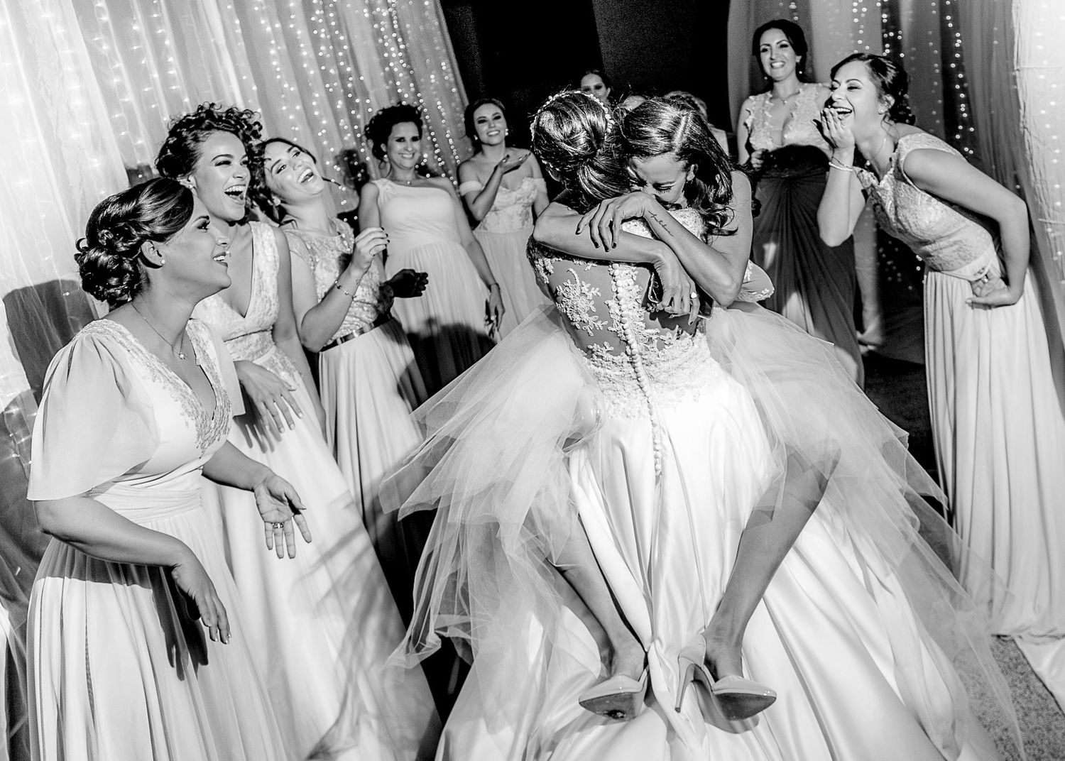 Group of bridesmaids in matching white dresses dancing and celebrating at wedding reception.