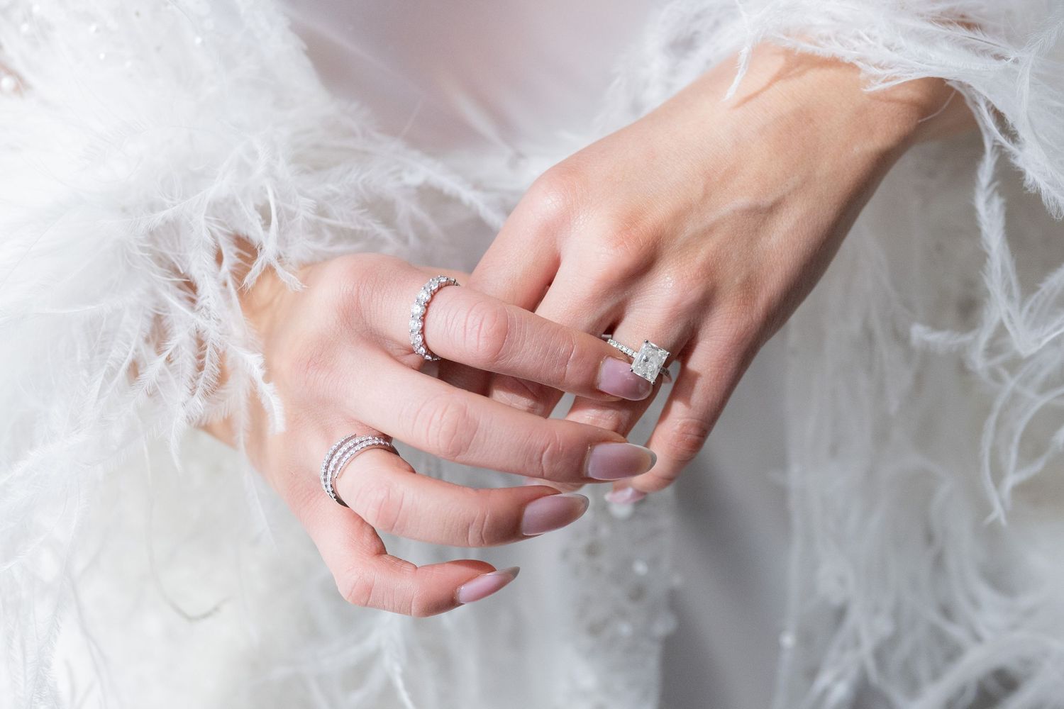 Elegant hands with wedding rings resting on white tulle fabric.