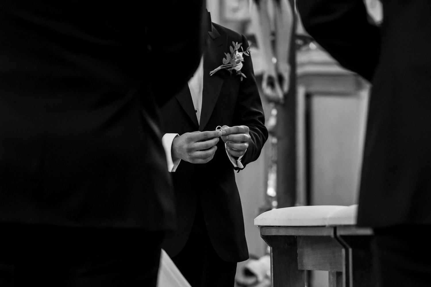 Groom holding wedding ring during ceremony in black and white photo.