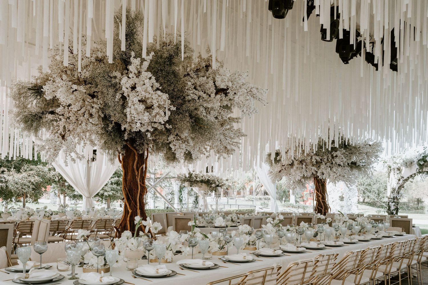Wedding reception tables set under dramatic white hanging decor and crystal chandeliers.